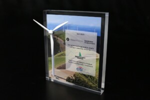 Clear acrylic deal toys stands upright on a dark surface, featuring an image of a wind turbine by the sea with overlaid investment and data text.