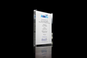 Transparent acrylic financial tombstones with arabic text and the logo "jazeera" at the top, displayed against a black background with reflection on the surface.